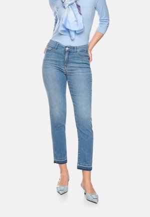 Woman wearing light blue three-quarter sleeve top, blue scarf, slim-fit cropped blue jeans, and light blue pointed-toe heels.