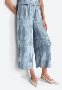 Light blue pleated culotte pants made from a shiny fabric, featuring a high waist and wide legs, paired with cream-colored slingback shoes.