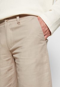 Beige op maat gemaakte broeken met een subtiel ruitpatroon, gemaakt van gladde stof. Voorzien van zijzakken en een enkele knoopsluiting.