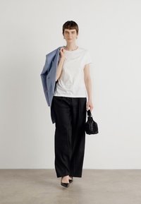 White t-shirt, loose black trousers, and pointed black heels. A light blue blazer draped over one shoulder, holding a small black bag.