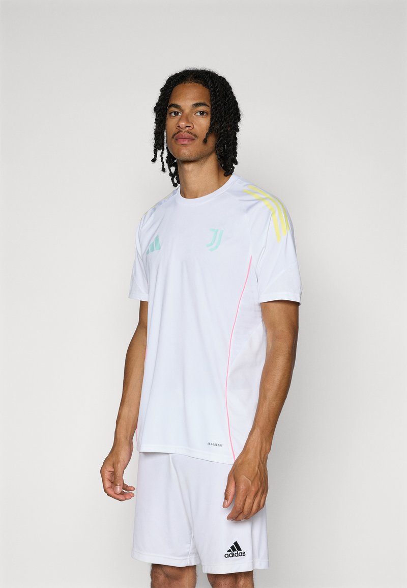 Fehér sportmez rövid ujjakkal és rózsaszín díszítéssel. Sárga Adidas csíkokkal a vállakon. Légáteresztő anyagból készült.