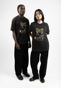 T-shirt grafiche nere presentano un design intricato con testo, indossate con pantaloni di velluto a coste neri e scarpe nere. Vestibilità semplice e casual per entrambi i portatori.