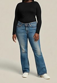 Jean évasé en denim bleu avec des accents délavés, doté d'une ceinture structurée, de cinq poches et de coutures apparentes, associé à un haut noir à manches longues.