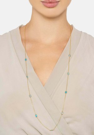 Gold chain necklace featuring turquoise rectangular stones evenly spaced along the length, set against a light-colored fabric backdrop.