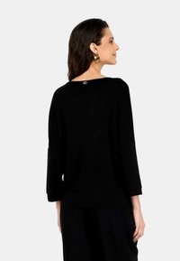 Top nero a maniche lunghe con scollo a barca, vestibilità rilassata, texture a coste e un piccolo logo sulla parte posteriore.