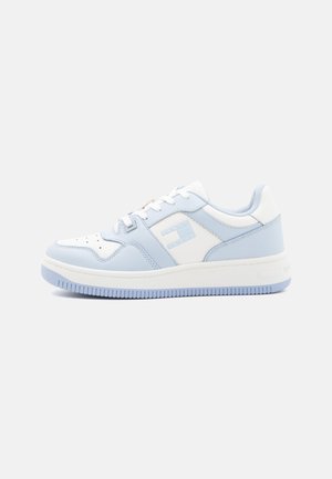 Zapatilla de color azul claro y blanco con parte superior de cuero suave, puntera perforada y suela de goma texturizada. Presenta un logo en el costado.