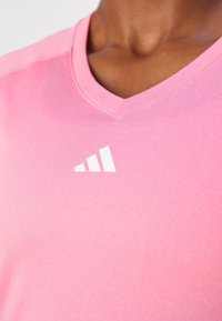 Pink v-neck athletic shirt with a smooth texture and white triangular logo on the chest. The fabric appears lightweight and breathable.
