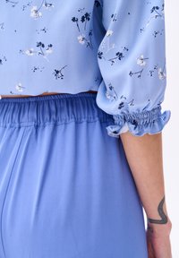 Lichtblauwe bloemetjesblouse met puffed mouwen en elastische manchetten. In combinatie met bijpassende losse, hoge taille blauwe broek.