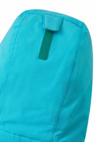 Türkisfarbener Stoff mit glatter Textur und einer genähten Naht, oben mit einer grünen Stoffschlaufe zur Befestigung versehen.