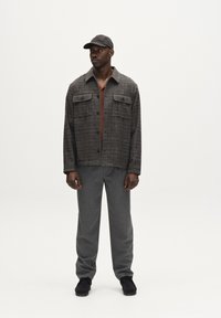 Hall lihtsalt halliruutudega jakk, millel on kaks rinna taskut, rustvärvi särk, hallid püksid ja mustad kingad, kõik paigutatud heledale taustale.