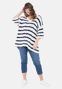Der Strickpullover hat einen V-Ausschnitt, kurze Ärmel und horizontale Streifen in Marineblau und Creme. Kombiniert mit cropped blauen Jeans und weißen Turnschuhen.