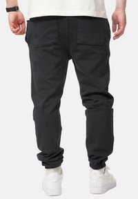 Schwarze Baumwoll-Jogginghosen mit elastischem Bund und Bündchen, ausgestattet mit zwei Gesäßtaschen und einem entspannten Schnitt. Kombiniert mit weißen Sneakern.