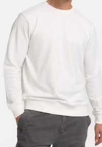 Sweat-shirt blanc à col ras du cou avec manches longues, fabriqué en matériau doux. Caractérisé par un col et des poignets côtelés avec un design simple.