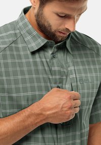 Groen geruit overhemd met korte mouwen en een button-down kraag, voorzien van witte rasterlijnen en een linkse borstzak. Zachte textuur en casual ontwerp.