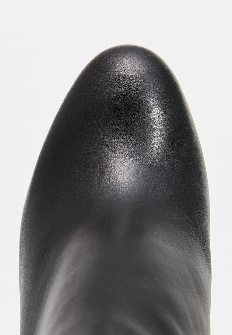 Bottine en cuir noir avec une texture lisse, un bout pointu et un design épuré et minimaliste. Aucun matériel ni motif visible.