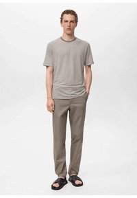Camicia a maniche corte a righe beige e bianca, abbinata a pantaloni dritti grigio chiaro e sandali neri a scivolo, caratterizzata da una vestibilità comoda.