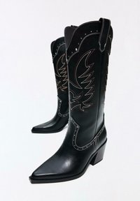 Zwarte leren cowboylaarzen met puntige neuzen, gedetailleerde stiksels en decoratieve arendpatronen. Voorzien van een blokhak en een geschulpte bovenkant.