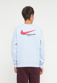 Light blue sweatshirt with a crew neckline, featuring a large red Nike Swoosh and the text "Nike Athletic Dept. Just Do It." on the back.
