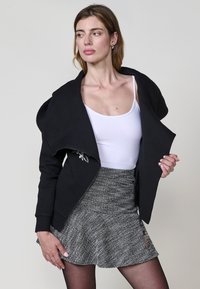 Chaqueta negra con cremallera, con un diseño texturizado de espiga y cuello sobredimensionado, combinada con una falda gris acampanada que presenta un patrón sutil.
