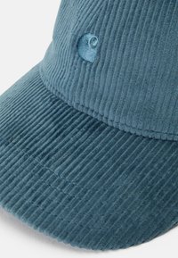Căciulă din fâșie albastră cu o suprafață texturată, prezentând dungi verticale și un mic logo brodat pe față.