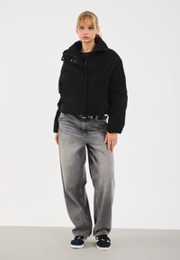 Svart kordfløyd cropped jakke med frontlommer, brukt over en svart topp og oversized falmet grå jeans. Modellen har på seg mørke joggesko.