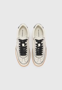 White leather sneakers featuring black stitching, black laces, and a gum sole. The interior has a logo printed on a beige background.