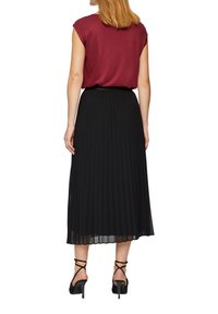 Haut ajusté bordeaux à manches courtes associé à une longue jupe plissée noire et des talons noirs à brides. Design de tenue moderne et fluide.