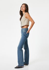 Beige kort topp med rundad nederkant, ihop med vida blå denimjeans. Mörka spetsiga skor med spänne synliga.