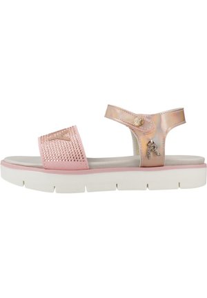 Sandale rose avec une semelle blanche plate, présentant une sangle irisée et brillante ainsi qu'un design clouté sur le dessus. Matériel décoratif inclus.