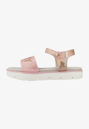 Sandale rose avec une semelle blanche plate, présentant une sangle irisée et brillante ainsi qu'un design clouté sur le dessus. Matériel décoratif inclus.