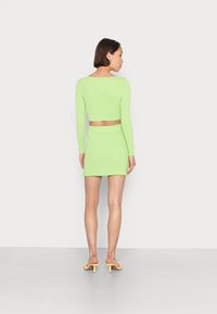 Conjunto de duas peças com um top cropped em verde limão brilhante com mangas longas e uma saia mini coordenada com a bainha desfiada.