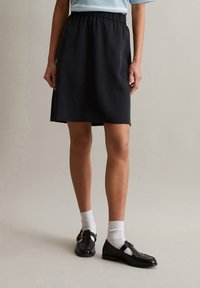 Schwarze knielange Röcke mit elastischem Taillengummi, glatter Textur und einfachem Design. Getragen mit schwarzen Schuhen und weißen Socken.