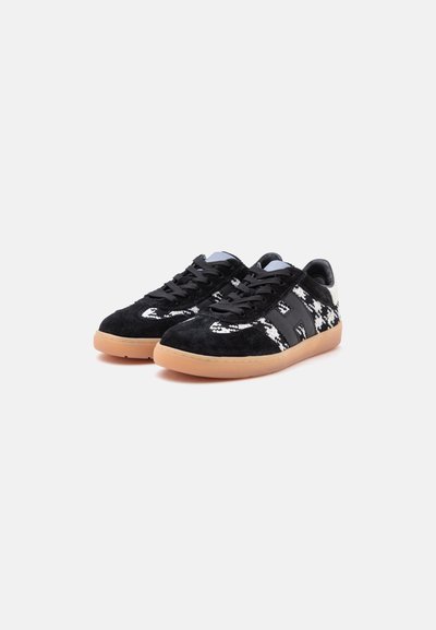 Paire de baskets à motifs noir et blanc avec des lacets noirs et des semelles en caoutchouc beige sur un fond clair.