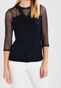 Granatowa bluzka z przezroczystymi rękawami 3/4 w groszki, koronkowymi detalami przy dekolcie oraz dopasowanym, jednolitym dołem.