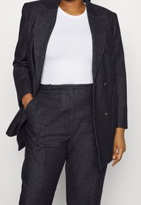 Donkergrijze op maat gemaakte blazer van gestructureerde stof, met een dubbelzijdig ontwerp en zijzakken, gecombineerd met een wit geribd top.
