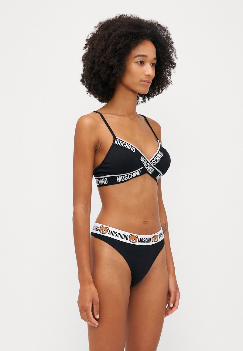 Black lingerie set featuring a bralette with a white logo band and matching thong with a bear design on the waistband. Soft fabric texture.