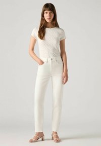 Witte jeans met rechte snit en twee zakken, gecombineerd met een fitted, kort mouw wit top met een subtiel bloemenpatroon. Lichtgekleurde sandalen.