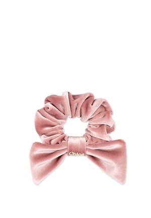 Coletero de terciopelo rosa con un gran lazo y un pequeño detalle de logo dorado sobre un fondo blanco liso.