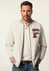 Giacca bomber bianca con colletto e polsini grigi, chiusura con zip e una patch ricamata marrone con la "P" e la scritta "Heritage" sul lato sinistro del petto.