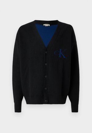 Fekete kardigán puha anyagból, V nyakkivágással, hosszú ujjal, hat gombbal, és egy kék "cK" logóval a bal oldalon.