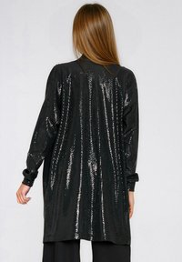 Długi czarny kardigan z cekinami, o luźnym kroju, z długimi rękawami i prostym dołem, odbijający światło dzięki błyszczącej fakturze.