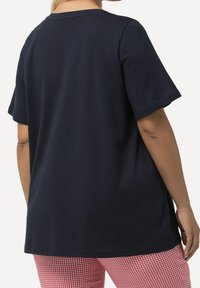 Tmavě modré bavlněné tričko s krátkými rukávy, kulatým výstřihem a volnějším střihem, doplněné červeno-bílými kalhotami se vzorem gingham.