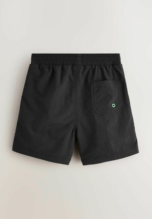 Shorts noirs avec une ceinture élastique, une poche arrière unique avec un accent de point vert, fabriqués en tissu léger.