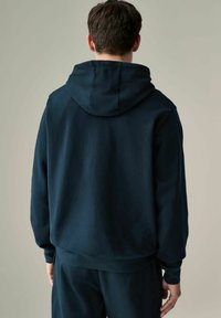 Sudadera azul marino con capucha ajustable, textura cepillada, puños y dobladillo acanalados, y un corte holgado; llevada con pantalones a juego.