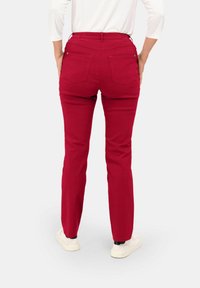 Rode stretchy broek met een aansluitende pasvorm, voorzien van een hoge tailleband, twee achterzakken en subtiele stikdetails. Draagt in combinatie met witte sneakers.
