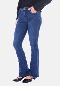 Jeans a zampa d'elefante blu in denim, con vita media, tasche frontali e una leggerissima texture sbiadita. Abbinati a scarpe nere con tacco basso.