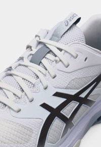 Κοντινό πλάνο λευκού παπουτσιού τρεξίματος Asics με μαύρο λογότυπο, λευκά κορδόνια και αναπνεύσιμο πλεκτό ύφασμα στο πάνω μέρος.