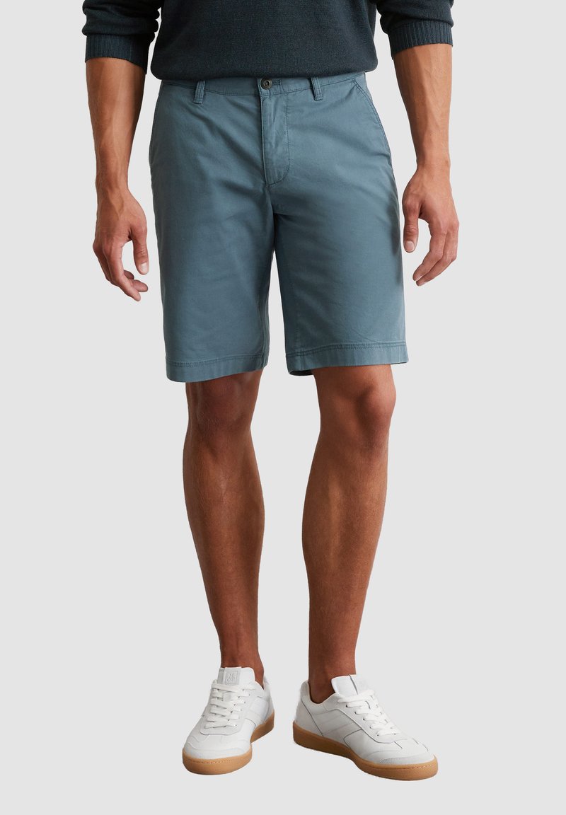 Shorts en coton bleu clair avec une coupe droite, poches avant et ourlet cousu. Portés avec des baskets blanches et un pull sombre.