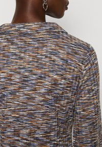 Maglietta a maniche lunghe con tessuto multicolore e testurizzato, caratterizzato da motivi ondulati in marrone, viola e bianco, e un design con colletto classico.