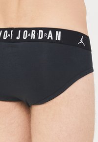 Schwarze Baumwollunterhose mit einem elastischen Bund, der das Wort "JORDAN" in weißen Buchstaben und ein Jumpman-Logo zeigt. Glatte Textur und eng anliegende Passform.